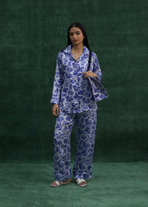 A woman wearing a blue silk pajama set with a leaf print, consisting of a long-sleeved top and pants, larosa